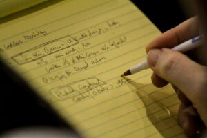 person holding white and black pen writing on yellow paper